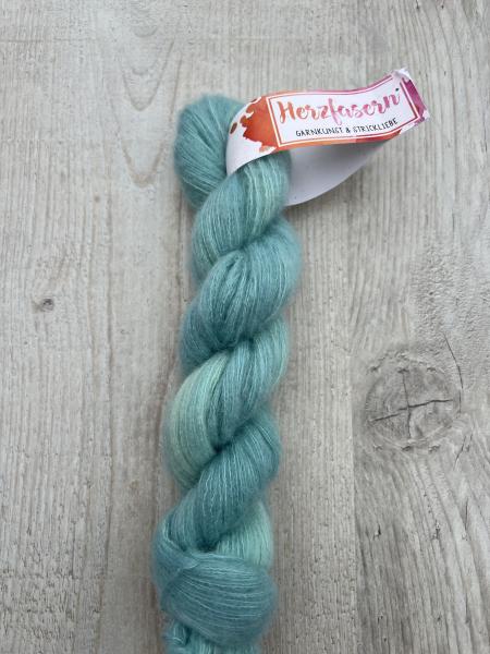 Abgebildet ist ein Strang Herzfasern No. 93 (Cashmere-Seiden-Lace) in einem changierenden Aquablau. Der Strang wirkt leicht, luftig und zeigt den charakteristischen feinen Glanz der Seidenmischung.